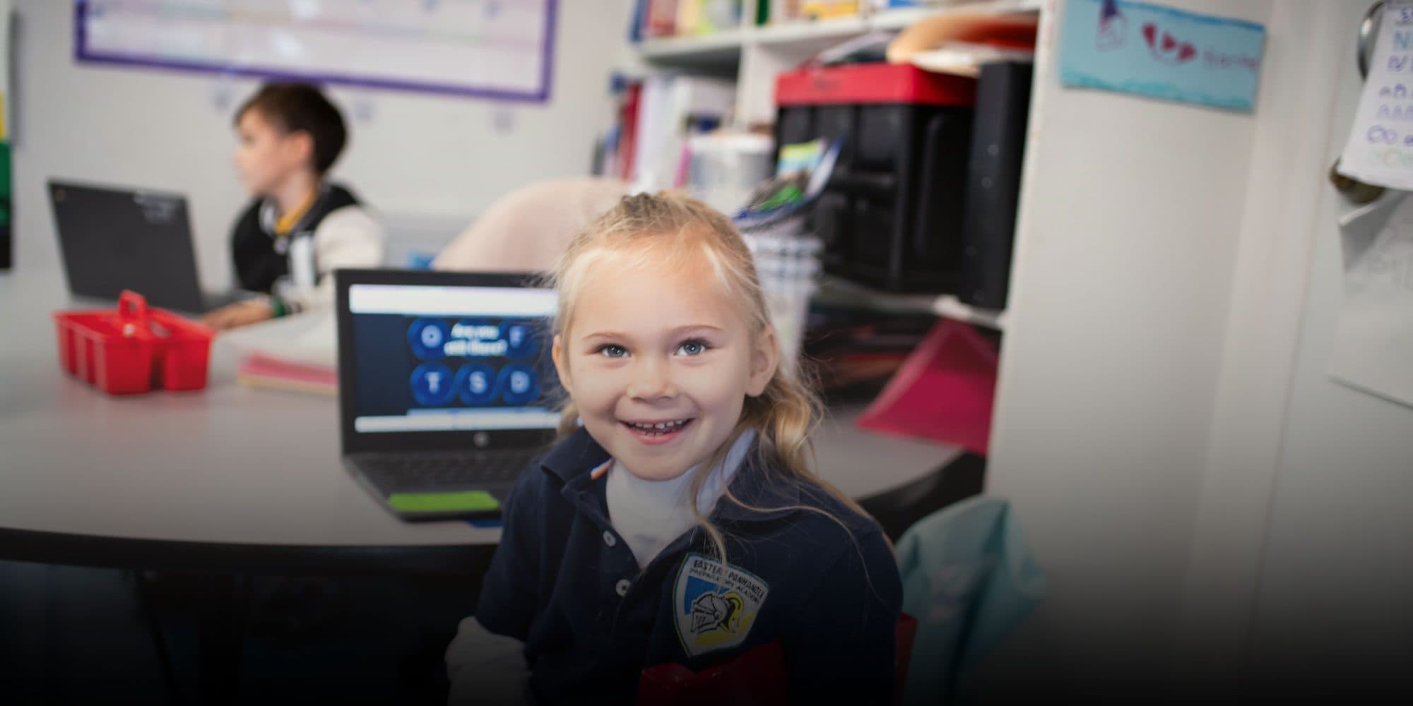 Smiling student in an EPPA uniform at a classroom table with a laptop.