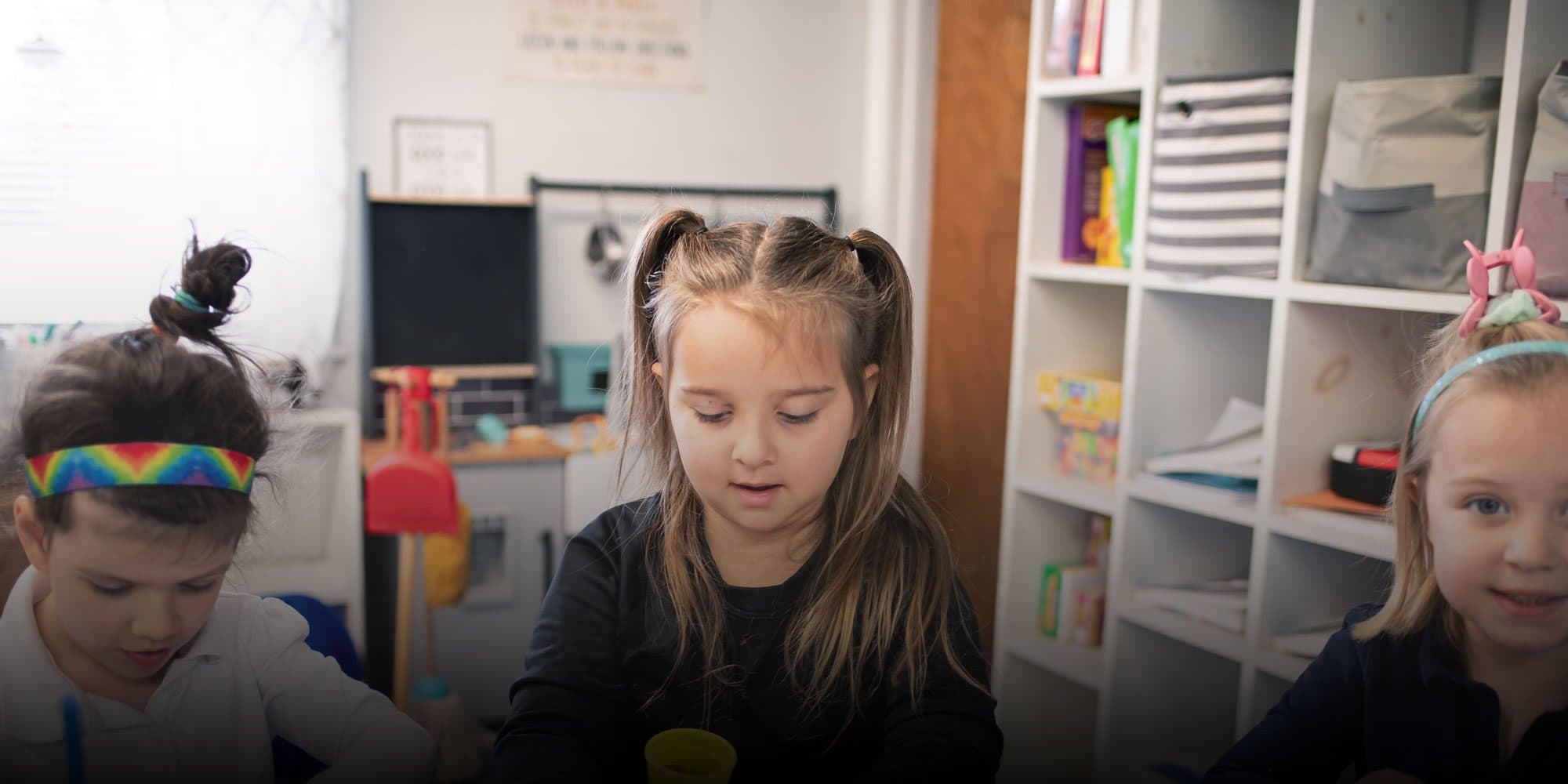 Three young students working together at a classroom table.